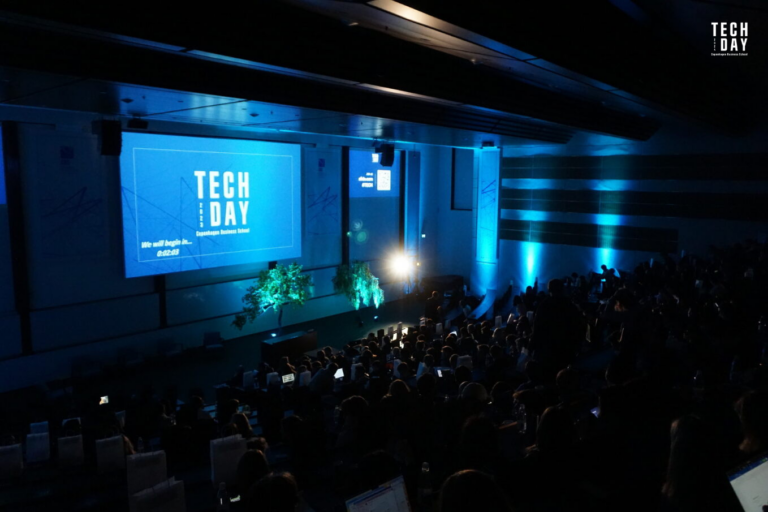 Attendees at Tech Day 2023 event in a dimly lit auditorium with a large screen displaying the event's name and countdown timer.